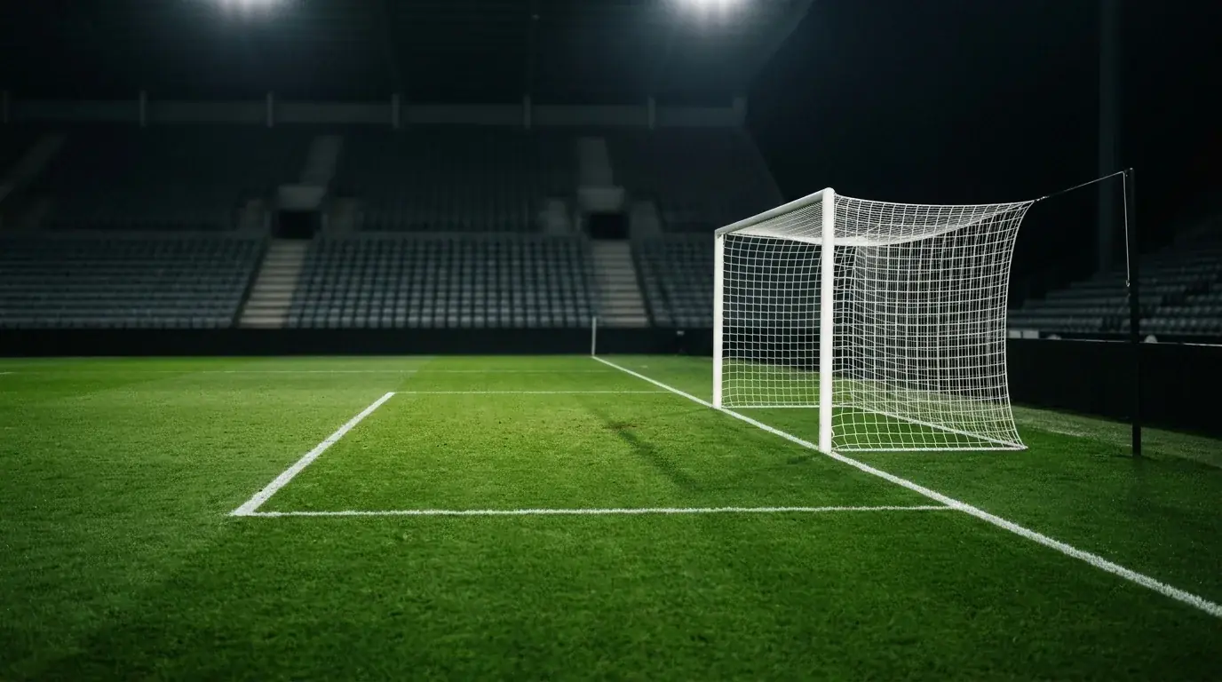 Ett fotbollsmål och en tom straffområdesyta fotograferad från sidan under strålkastarljus